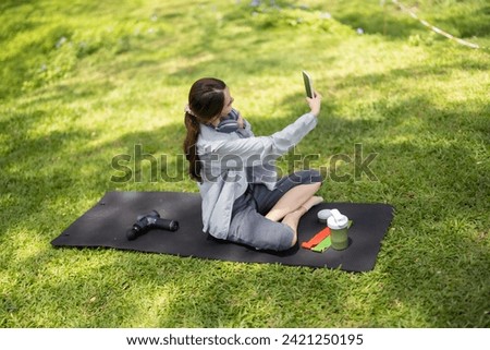 A female social media influencer is captured mid-conversation, showcasing a protein powder drink to her online audience while seated on a lush green lawn.