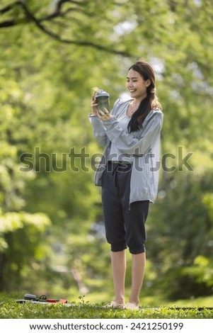 A female social media influencer is captured mid-conversation, showcasing a protein powder drink to her online audience while seated on a lush green lawn.