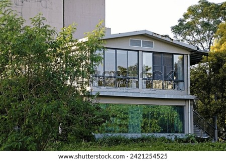 Close-up of a loft-style house in a green garden, in a park, coastal area, modern square house in nature. glass house in the garden, reflection, architectural space merging with nature, trees