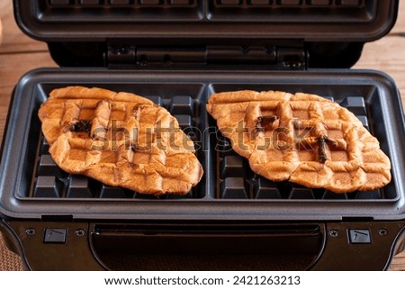 Croffle or croissant waffle in a waffle maker on a wooden board. Croissant as waffle