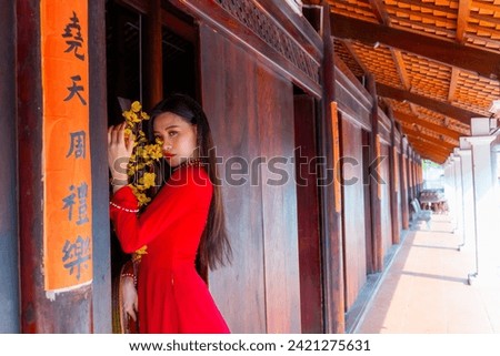 Vietnamese girl with Ao Dai dress standing in traditional house of Vietnam. Text in photo mean best wishes to family, happiness, prosperity, health. Tet holiday and New Year. Travel concept