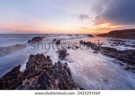 Lonely rocky beach with surf shortly after sunset, red and yellow tones in the sky, water movement in long exposure, depth effect - Location: Portugal, Azores, Corvo island