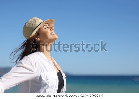 Side view portrait of a happy woman on the beach breathing fresh air wearing hat a summer sunny day Royalty-Free Stock Photo #2421295213