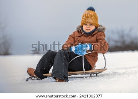 Portrait of cute boy resting on sled in winter outdoors.