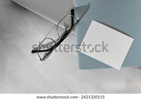 Minimal business brand template, blank paper business card mockup, light blue notepad, eyeglasses, laptop on marble table background, minimal aesthetic workspace, soft natural light and shadow.