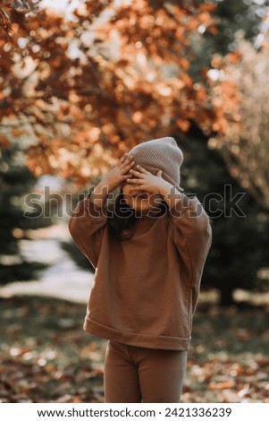 happy little brunette girl in a knitted hat walks in the park in autumn. High quality photo