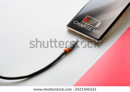 Trendy cell phone - smartphone and wire with usb type-c connector on white and red background. Charge me! AI's request for recharging. Copy space. Photo. Selective focus. Close-up