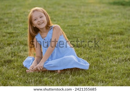 beautiful little girl with long blonde hair is sitting on the lawn in summer
