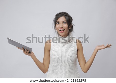 Photo of positive Pakistani intelligent woman in white sleeveless sweater holding tablet presenting offer and empty space isolated on white background