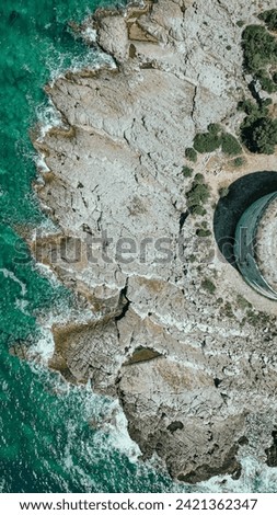 Aerial View of Rocky Shoreline Meeting Turquoise Sea Royalty-Free Stock Photo #2421362347