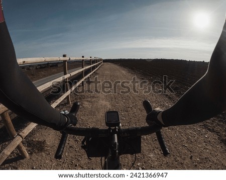 Riding on a gravel bicycle on a cycling way with a fence next to an asphalt road rider point of view