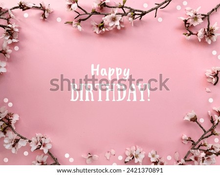 Text Happy Birthday in a frame with blossoming spring almond flowers on a pink paper background.