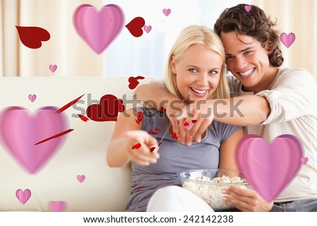 Cute couple watching TV while eating popcorn against love heart pattern