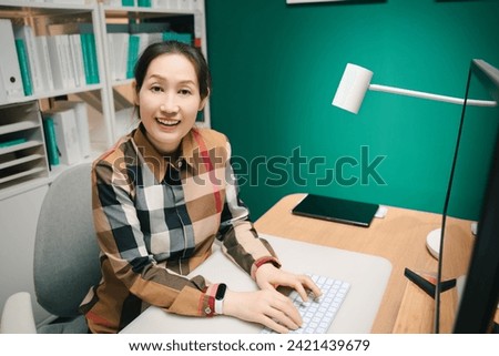 A photo of a smiley Asian woman in front of the computer table