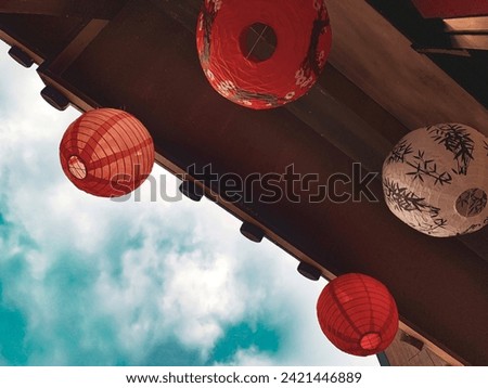 Bottom view of lanterns hanging from the wooden roof with the cloudy blue sky