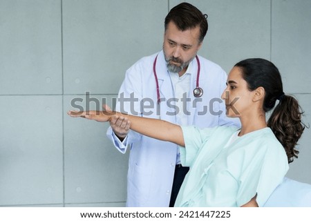 physiotherapist examines the extended arm of a female patient, focusing on her physical therapy. Intense concentration is shown by a therapist assessing a patient's arm mobility in a medical setting. Royalty-Free Stock Photo #2421447225