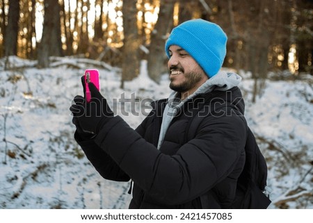Young hispanic black man taking a picture outdoor with a smartphone. The guy is a hiker walking on a hiking trail during winter time