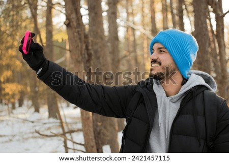 Latin black man taking a selfie, smiling and resting during a hiking day, he's in a New Jersey forest, holding a smartphone, trees background