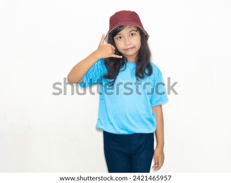 Girl in blue with a red hat signals, "Call me," portraying a playful invitation. Royalty-Free Stock Photo #2421465957