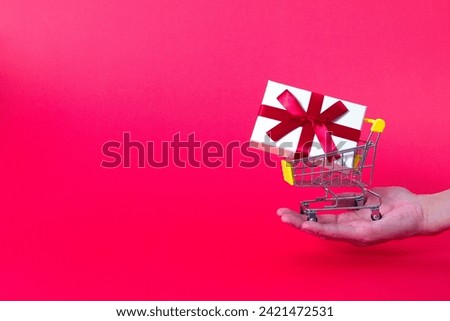 The image on the right shows a miniature shopping cart holding a present box in the palm of your hand. Text title space. Imaged as a gift for Christmas, Valentine's Day, or a birthday.