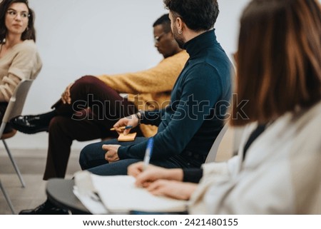 Focused professionals listening attentively in a business workshop, with notes and coworker interaction in a casual office setting.
