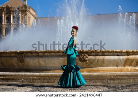 Beautiful young woman in a green frilly suit with a flower on her head. The woman is dancing flamenco and is in the most famous square in seville, spain, in front of its central fountain Royalty-Free Stock Photo #2421498447