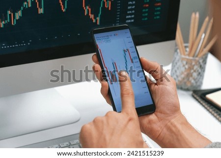 Smart stock investors pointing on screen with smartphone for market stock exchange along with laptop screen in highest dynamic investment rate, focusing data planning at modern workplace. Pecuniary.