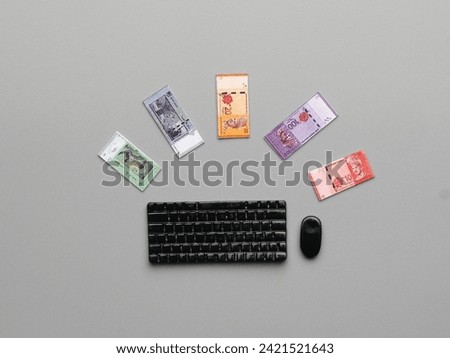 Flatlay picture of miniature keyboard and mouse fake miniature Ringgit Malaysia money on grey background.