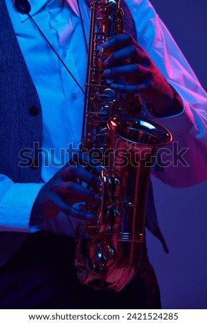 Cropped photo of African-American jazz-man playing saxophone, wind instrument against gradient background in mixed neon light. Concept of classical musical instrument, concerts and festivals. Ad Royalty-Free Stock Photo #2421524285