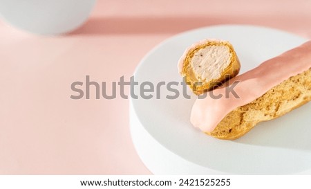 Eclair with strawberry custard cutaway and pink icing on pastel pink background. Delicious eclair with cream filling covered with pink melted glaze. Close up. Cafe menu, confectionery special offer Royalty-Free Stock Photo #2421525255