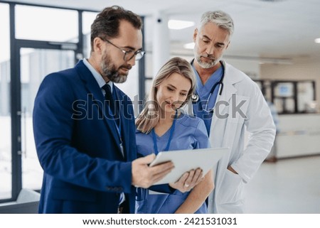 Pharmaceutical sales representative talking with doctors in medical building, presenting new medication on tablet. Hospital director, manager in modern clinic with doctor and nurse. Royalty-Free Stock Photo #2421531031