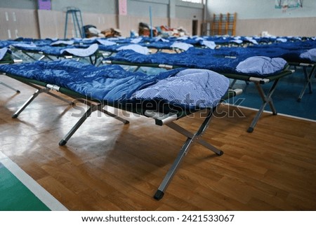 Cots with sleeping bags are placed in the school gym during an emergency Royalty-Free Stock Photo #2421533067
