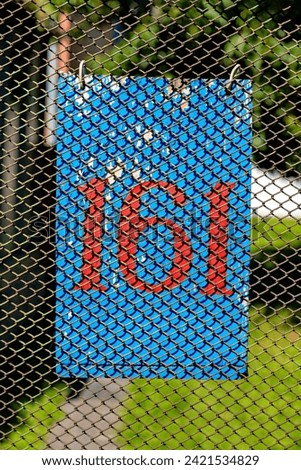 There is a blue sign with the number 161 in red hanging on the fence.
