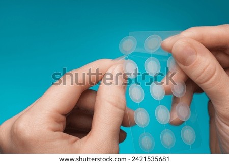 Close-up round acne patch on finger on blue background. Acne patches for treatment of pimple and rosacea close-up. Facial rejuvenation cleansing cosmetology Royalty-Free Stock Photo #2421535681