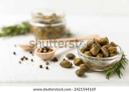 Capers in a bowl on a wooden kitchen table. Capers with sea salt and rosemary. Pickled capers.Mediterranean cuisine ingredient. Organic spices and seasonings. Copy space. Royalty-Free Stock Photo #2421544169