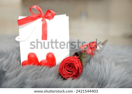 Festive background from gift bag with bow, stabilized rose and hearts on gray fur for valentine's day, mother's day, birthday