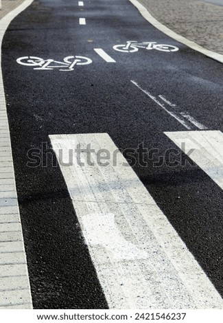 From above of empty asphalt road with white boundary lines and pedestrians zebra crossing markings while bicycle image impressions painted on black surface with cycling directions