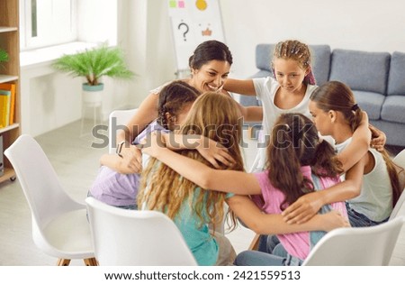 Teenage school girls sitting in a circle and hugging with their friendly smiling teacher or psychologist woman during therapy session group. Kids mental health and psychotherapy concept. Royalty-Free Stock Photo #2421559513