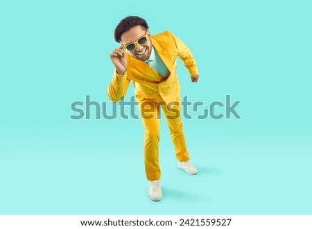 Full length portrait of funny friendly happy smiling showman in yellow suit and sunglasses tilting looking at camera on turquoise background. Banner for advertisement, marketing with copy space.