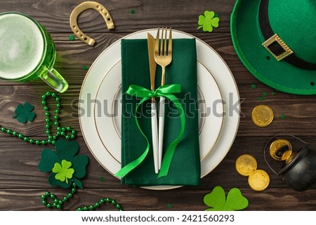 Join the St. Patrick's Day festivities at the bar. Top view of a table presentation with plate, cutlery, beer, leprechaun's hat, lucky horseshoe, pot of gold coins, trefoils against wooden background Royalty-Free Stock Photo #2421560293