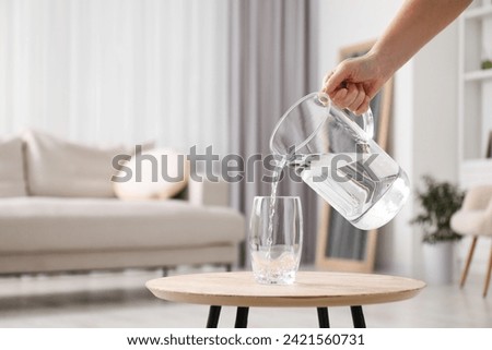 Woman pouring fresh water from jug into glass at wooden table indoors, closeup. Space for text Royalty-Free Stock Photo #2421560731