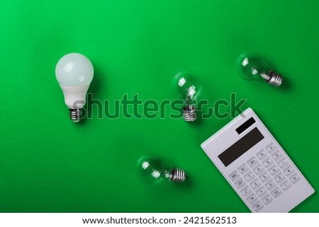 White calculator and incandescent lamps or LED bulb on green background. Concept showing the payment of electricity bills. The concept of savings electricity. Reducing the payment of utility bills.
