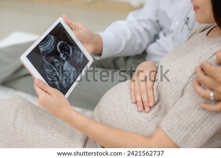 Picture of a pregnant woman and husband Asian couple looking at ultrasound images of their child Happy pregnant woman in the living room of her home before giving birth
