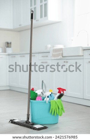 Mop and plastic bucket with different cleaning supplies in kitchen