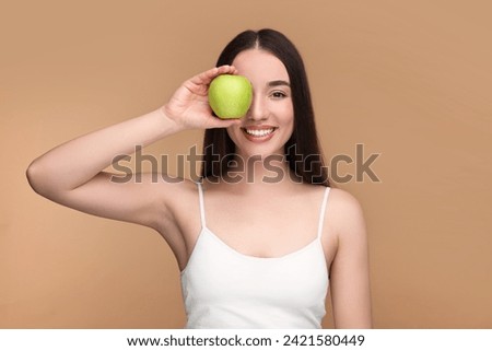 Beautiful young woman with apple on beige background
