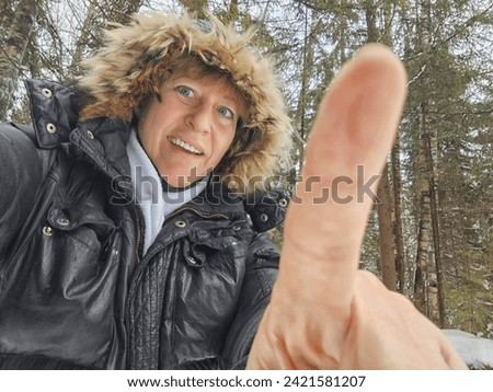 Happy, cheerful middle-aged woman in a warm jacket and a hood with fur taking selfie in winter outdoors. Female Traveler in Alaska, Lapland, Arctic, Siberia Royalty-Free Stock Photo #2421581207
