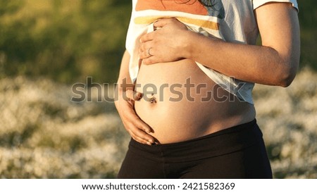 Portrait of a woman during the first months of pregnancy stroking her belly gently in nature in the sun in the family way Royalty-Free Stock Photo #2421582369
