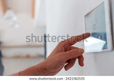 Close up of smart thermostat, adjusting, lowering heating temperature at home. Concept of sustainable, efficient, smart technology in home heating and thermostats. Royalty-Free Stock Photo #2421582535