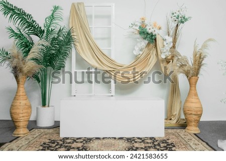 a stylish photo studio set with a golden scarf hanging from the window, floral decorations, and a box to sit on