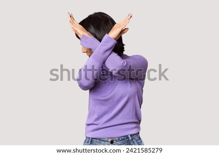 Young Hispanic woman with short black hair in studio keeping two arms crossed, denial concept.